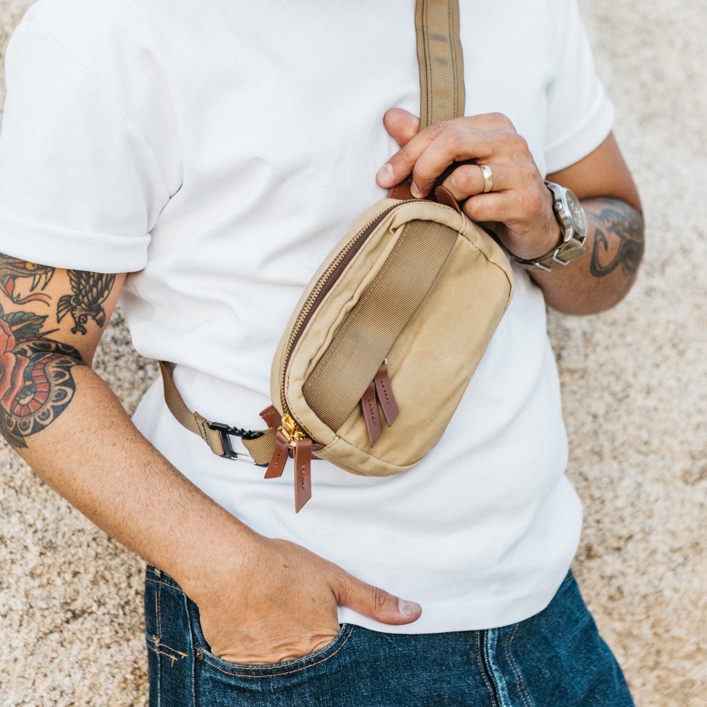 Tan canvas Canyon Crossbody Mini bag with brown leather zipper pulls and gold hardware, worn across the chest.