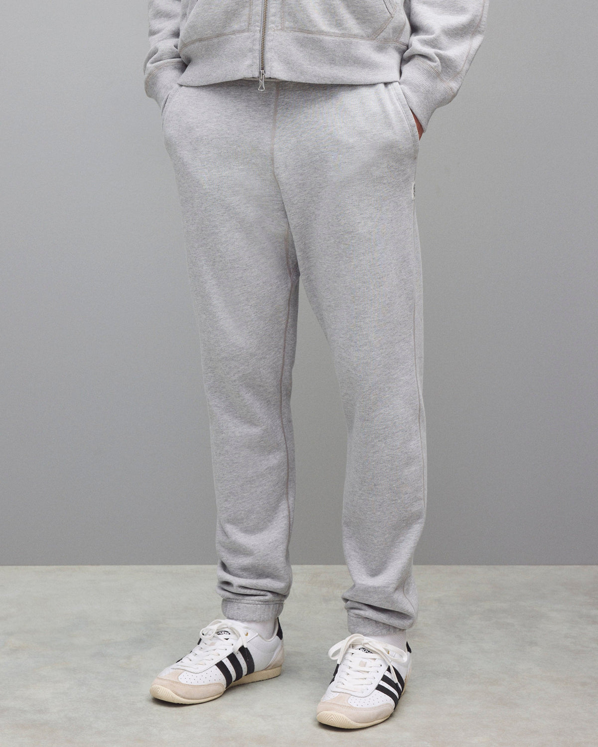 Midweight terry sweatpants in heather grey, styled with a matching zip-up hoodie and white sneakers.