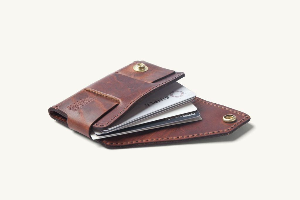 Cognac leather cardholder, open and angled, showing several credit cards and brass snap details.