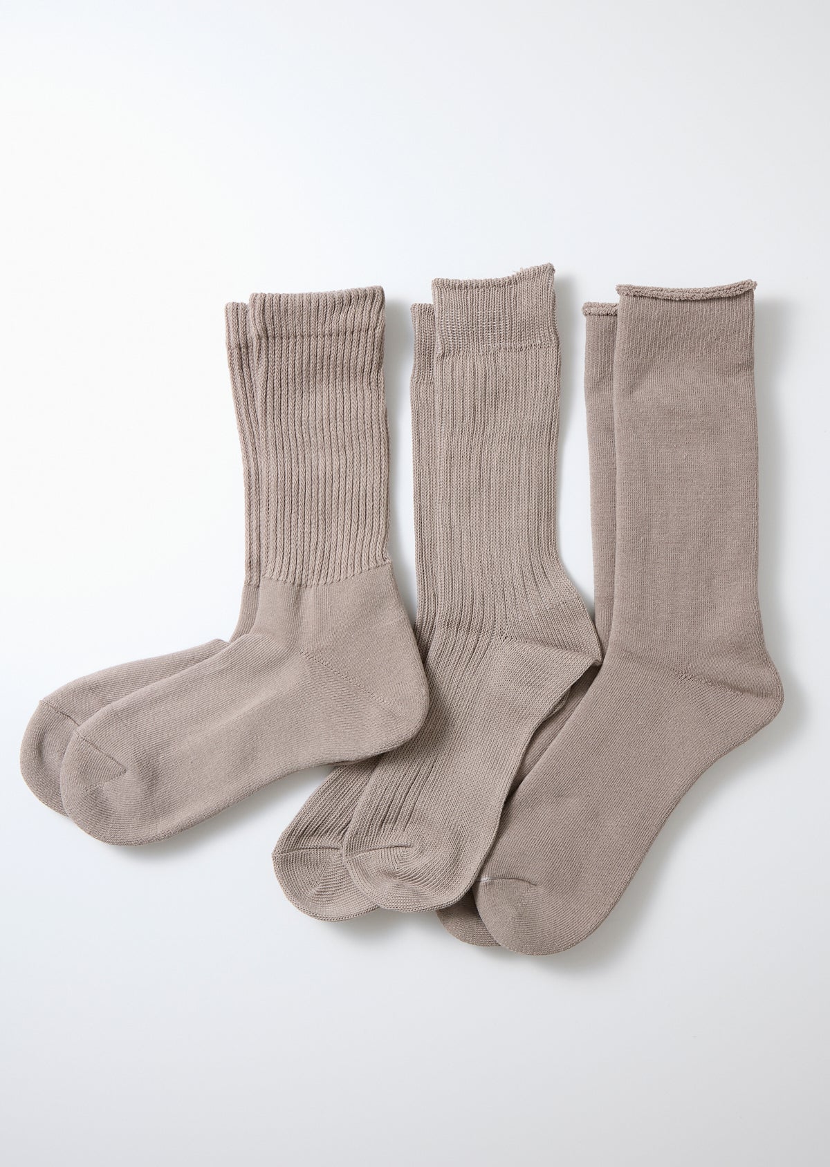 Three pairs of gray organic crew socks, one ribbed, one mixed textured, and one smooth, lying flat on white.
