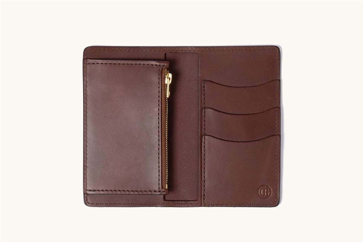 Cognac leather bifold wallet, open, revealing a zippered pouch, three card slots, and a small embossed logo.
