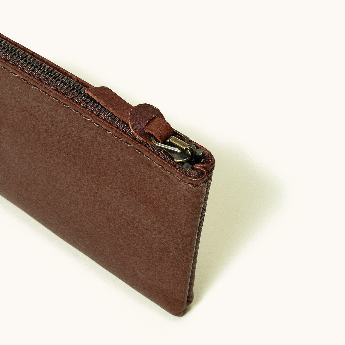 Cognac brown leather universal zip wallet with a brass zipper, shown at an angle.