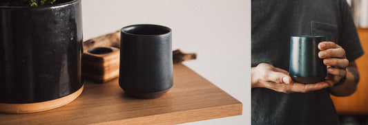 Hands cradle a steaming dark ceramic mug beside a wooden tray with tea canister, evoking calm tea ritual.