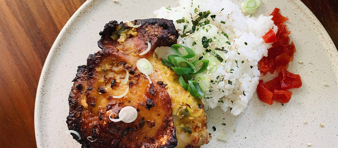 Crispy roasted chicken with white rice, green onions, sesame seeds, and red peppers on a speckled plate.