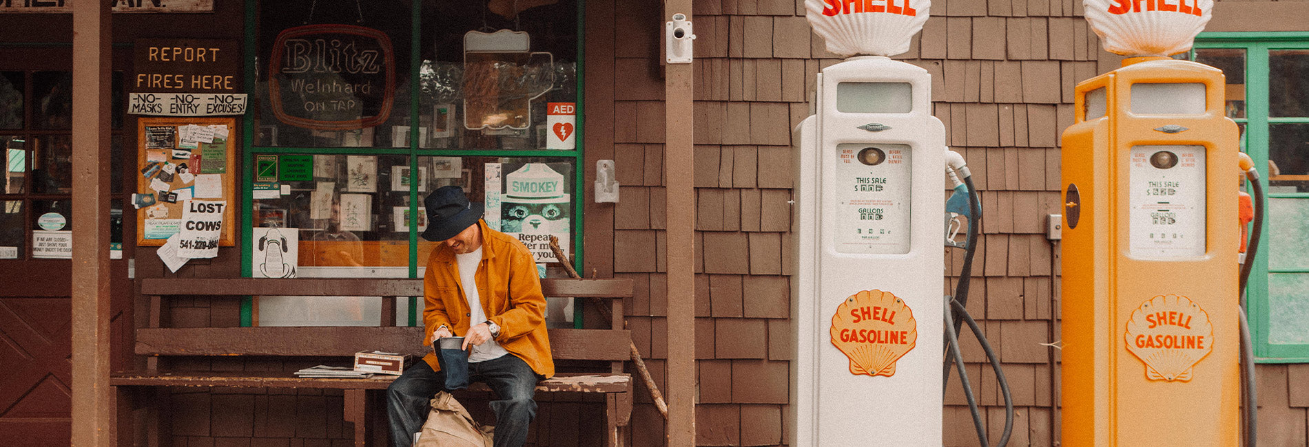 Retro gas station scene with man in mustard jacket, vintage Shell pumps, and rustic roadside charm.