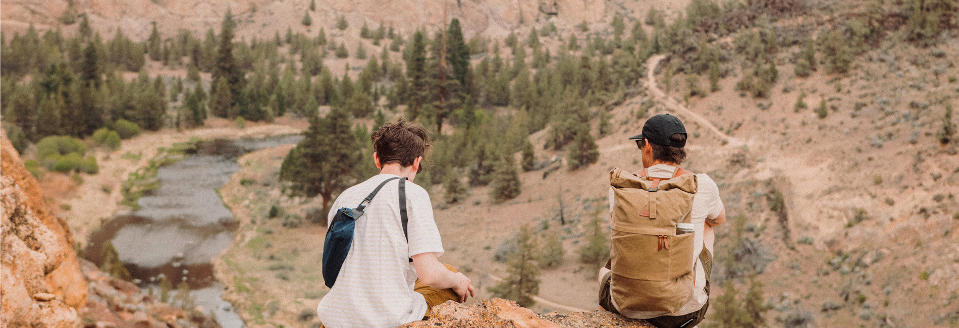Two hikers with canvas backpacks overlook a rugged canyon trail, embodying adventure and outdoor exploration.