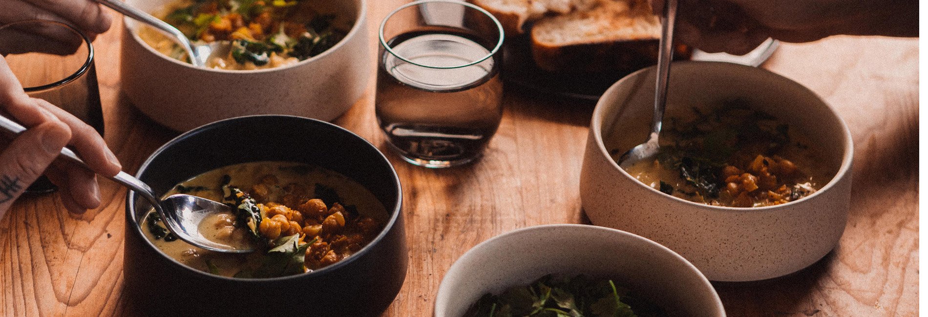 A dinner setting on a wooden table with spoons entering ceramic bowls filled with chickpea curry.