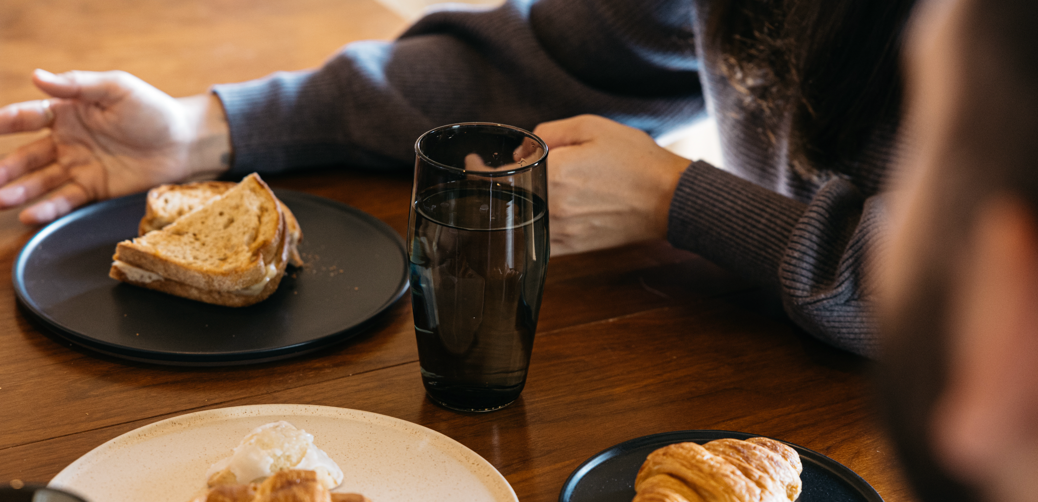 Minimalist homeware collection: matte black plates, smoked glass, warm wood table, cozy breakfast scene.