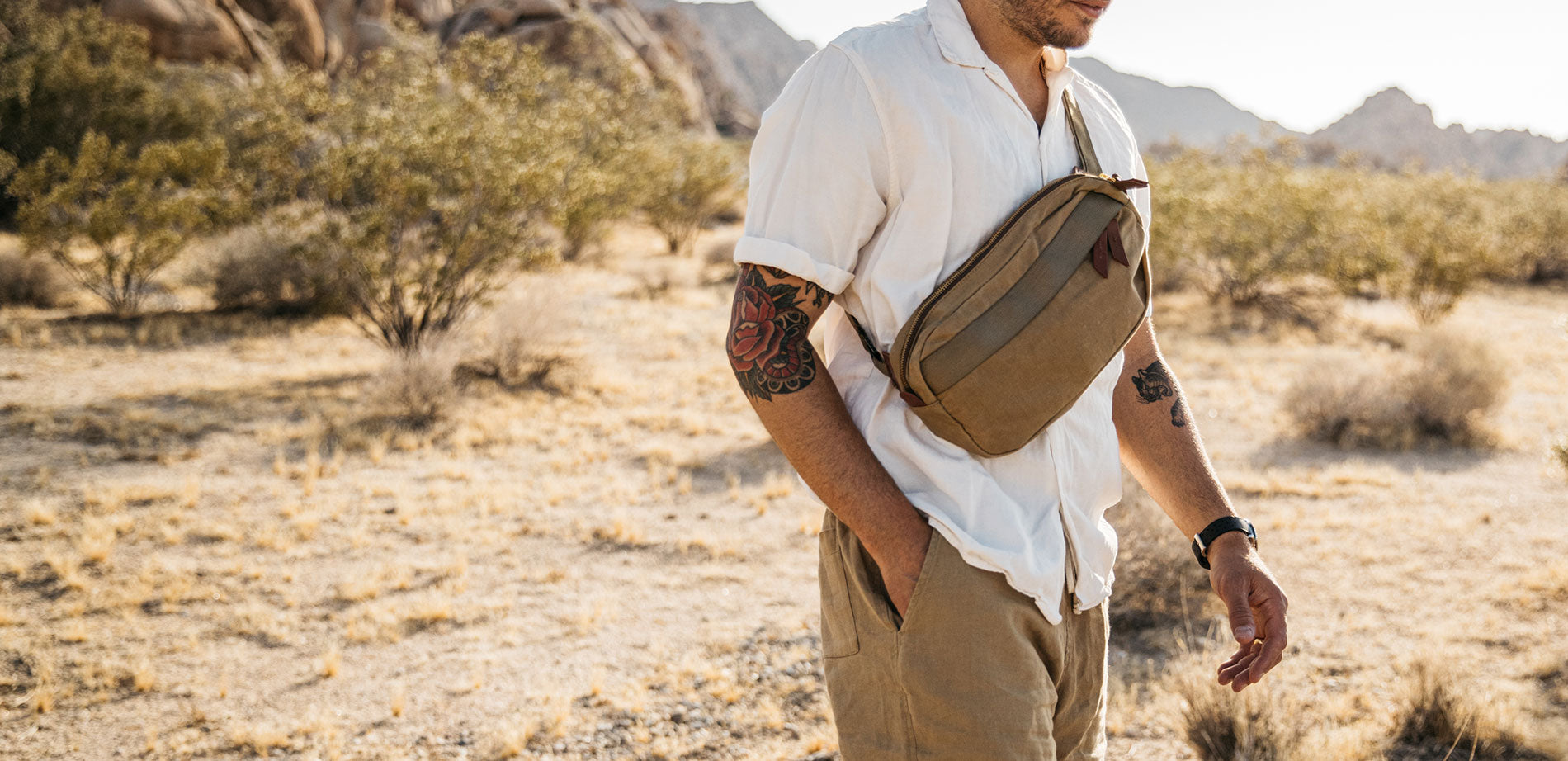 Man in desert landscape wearing tan crossbody pack with white shirt and khaki pants, embodying adventure-ready style.