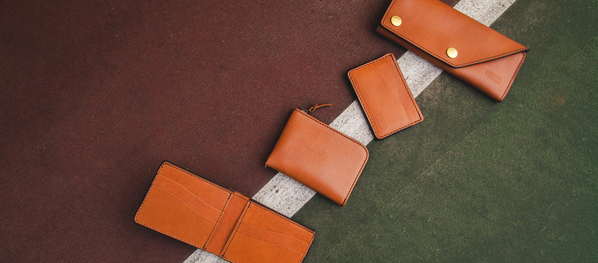 Rich saddle tan leather wallets and card holders arranged on textured asphalt, showcasing timeless craftsmanship and urban sophistication.