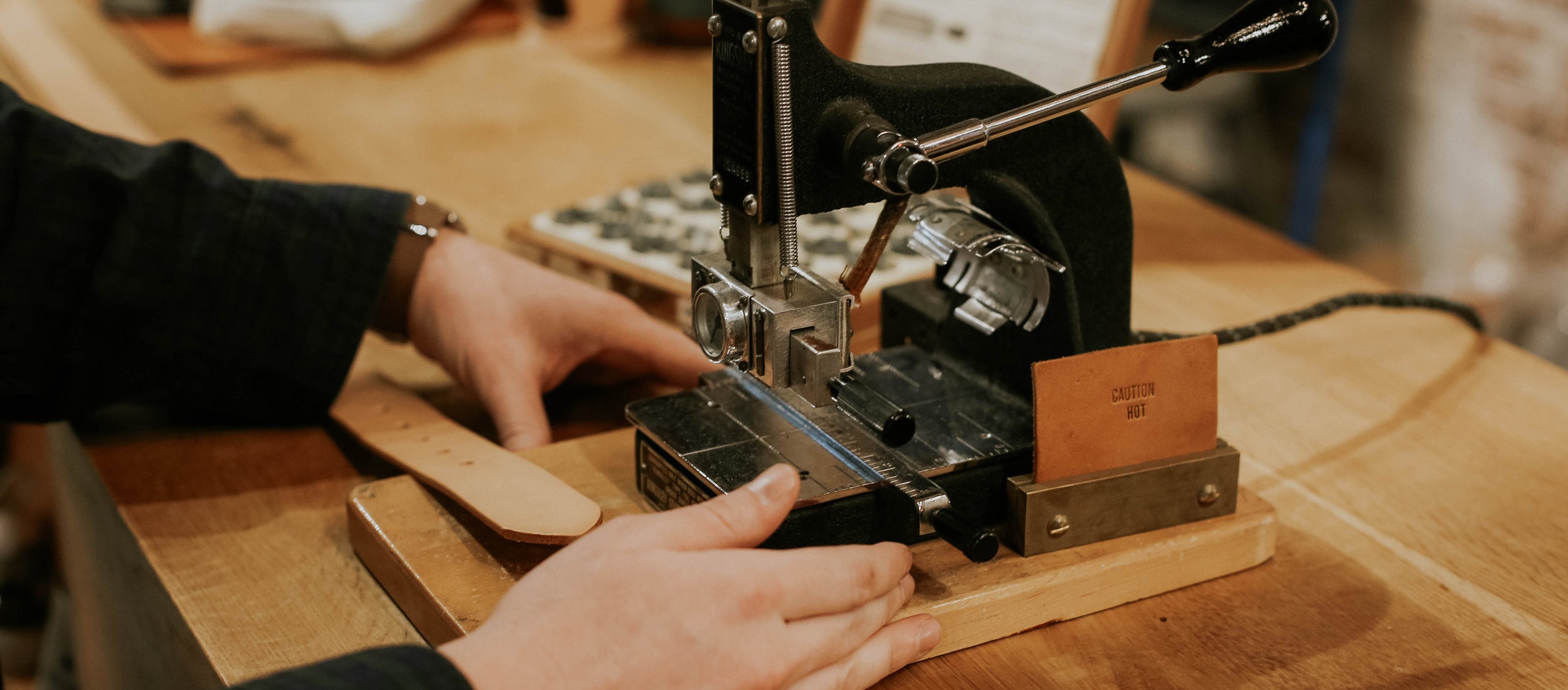 Hands crafting personalized leather goods with vintage monogramming press, warm wood tones, artisanal holiday gifts.