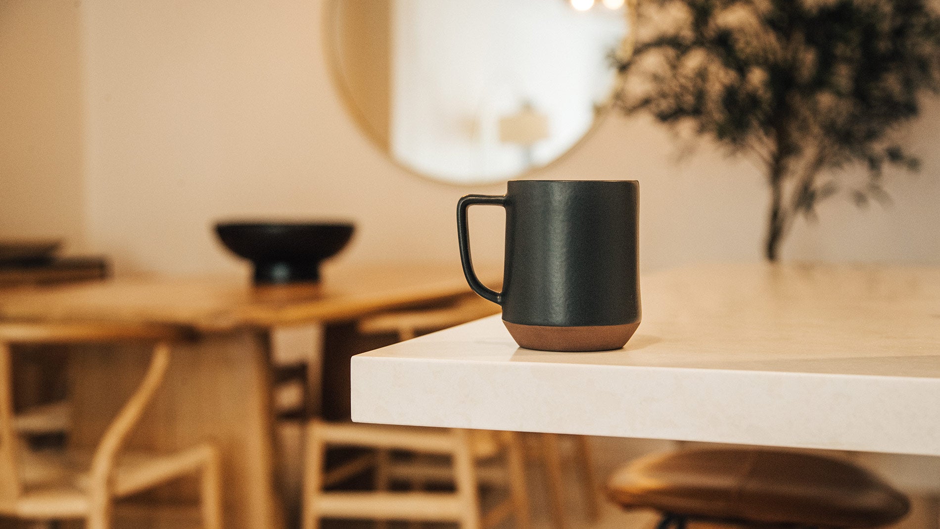 Matte black ceramic mug with terracotta base on marble countertop, warm minimalist kitchen setting, stylish home gifts under $75
