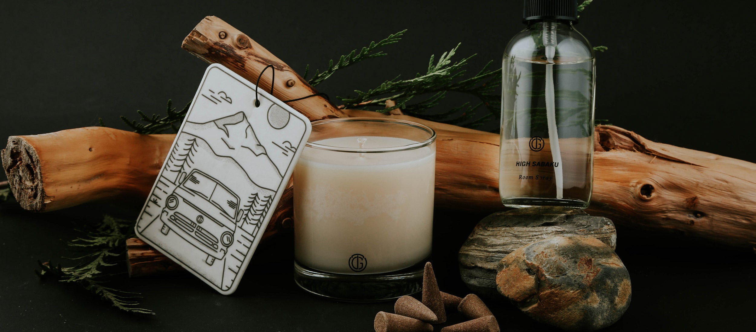 Tanner Goods Essentials: minimalist candle, room spray, and mountain-themed tag on rustic wood and stone, earthy tones, outdoor-inspired lifestyle.