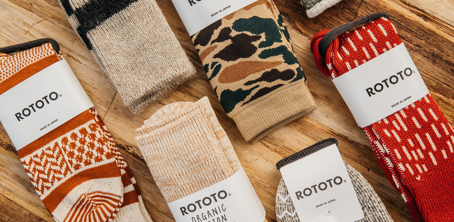 Rototo socks in earthy tones and bold patterns, made in Japan, styled on rustic wood.