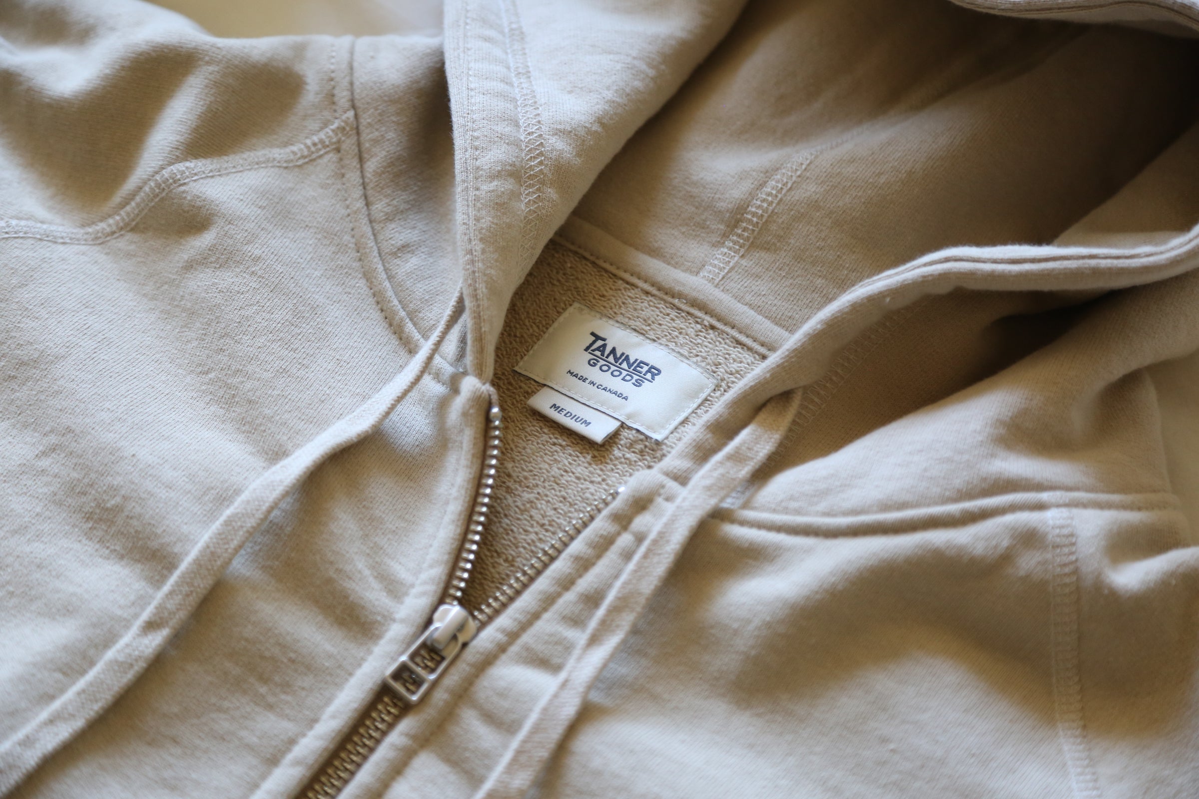 Cream-colored zip hoodie with Tanner Goods label, soft texture, minimalist design, cozy everyday wear.