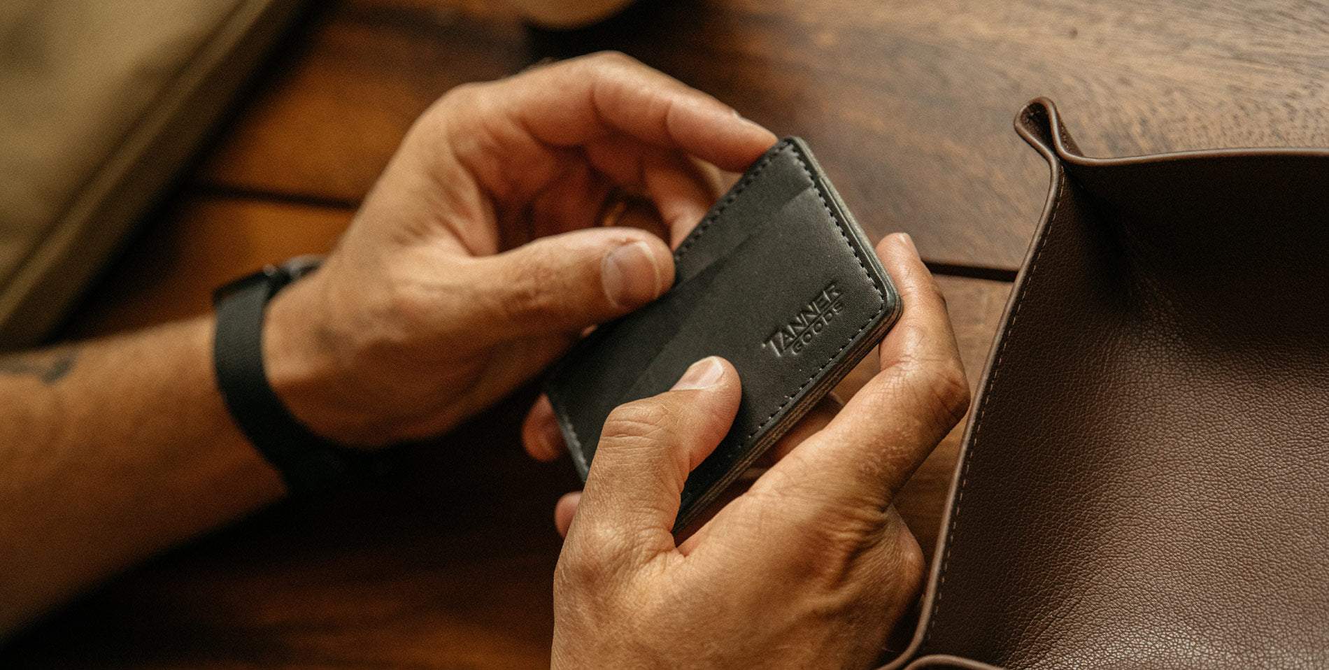 Hands holding sleek black leather wallet with embossed brand, warm wood backdrop, minimalist luxury design.