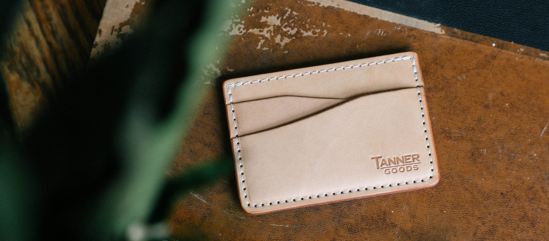 Tan leather cardholder with white stitching on rustic wood, showcasing Tanner Goods’ minimalist, handcrafted style.