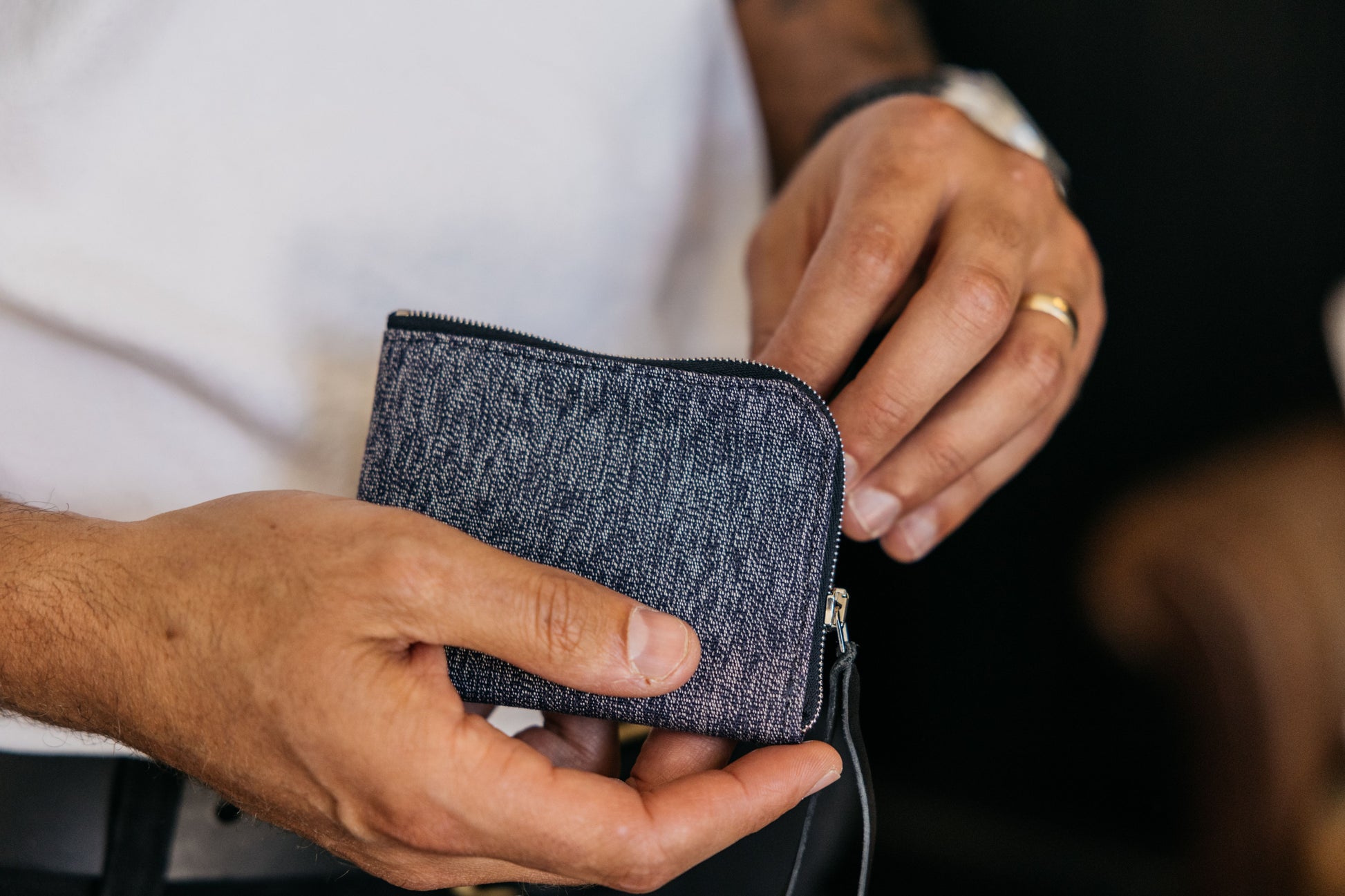 Indigo Salt and Pepper textile zip wallet, held in hands with its zipper partially open, showing a woven texture.