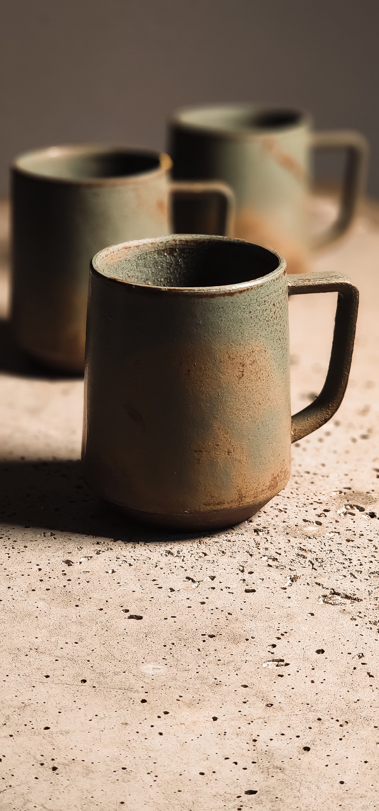 Earthy green and brown ceramic standard mug with a rustic, textured finish on a speckled surface.