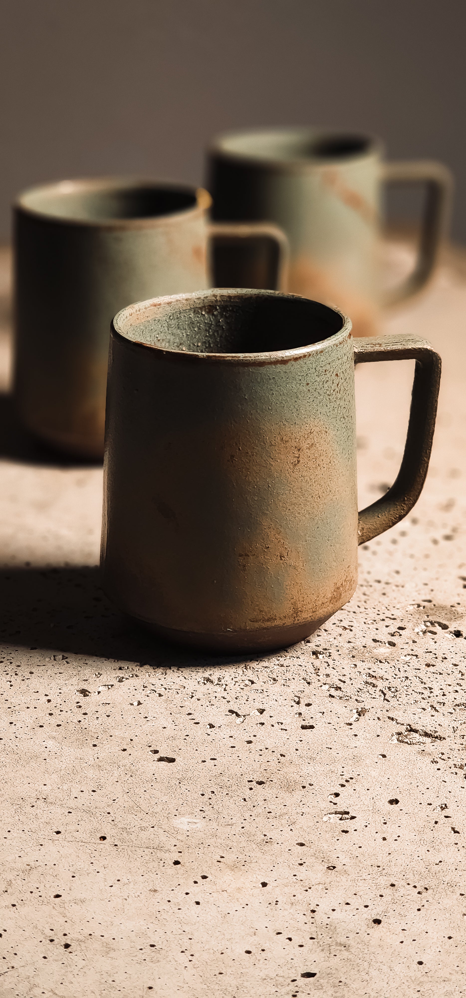 Earthy green and brown ceramic standard mug with a rustic, textured finish on a speckled surface.
