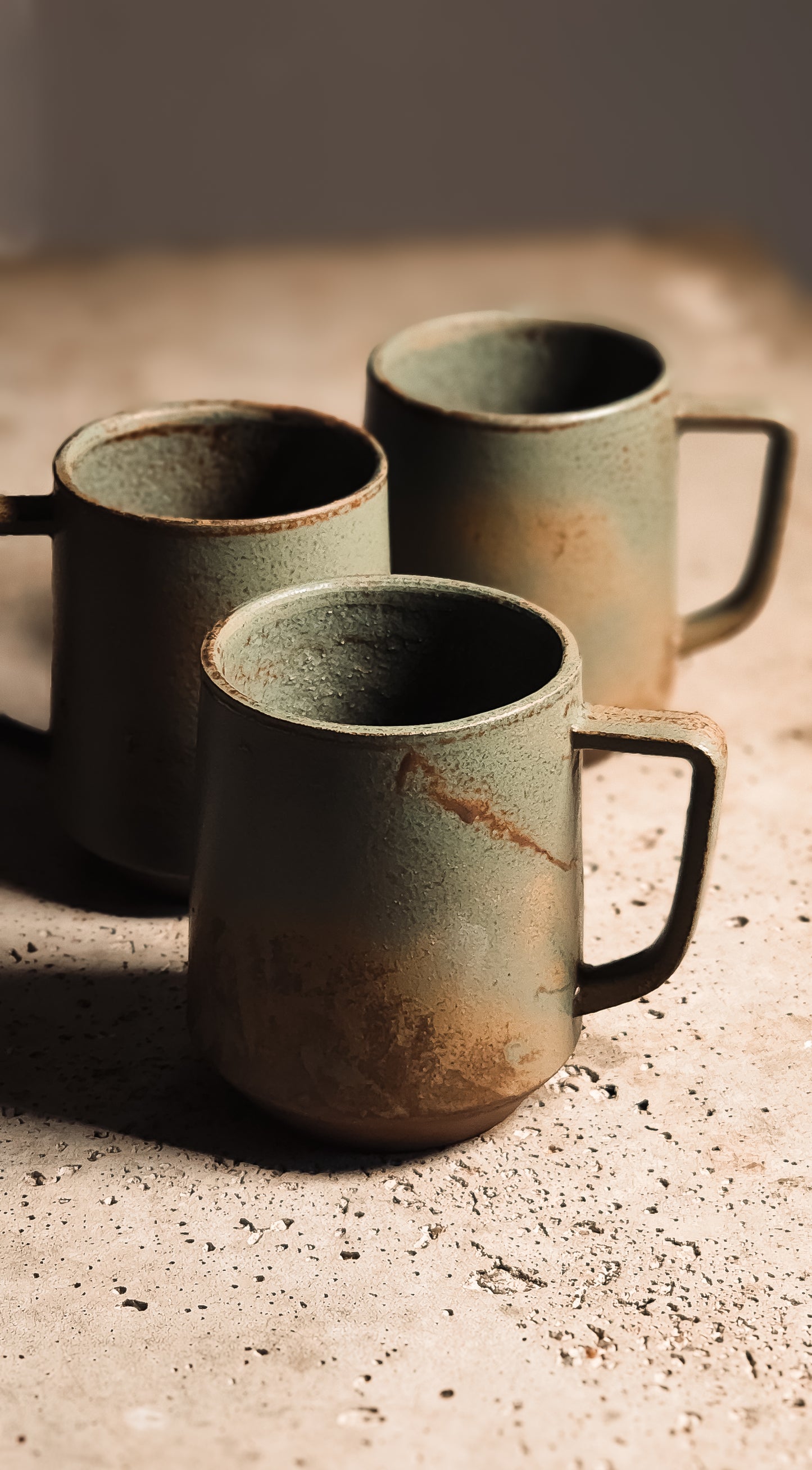 Textured sage green stoneware mug with earthy brown ombré and dark handle on a speckled surface.