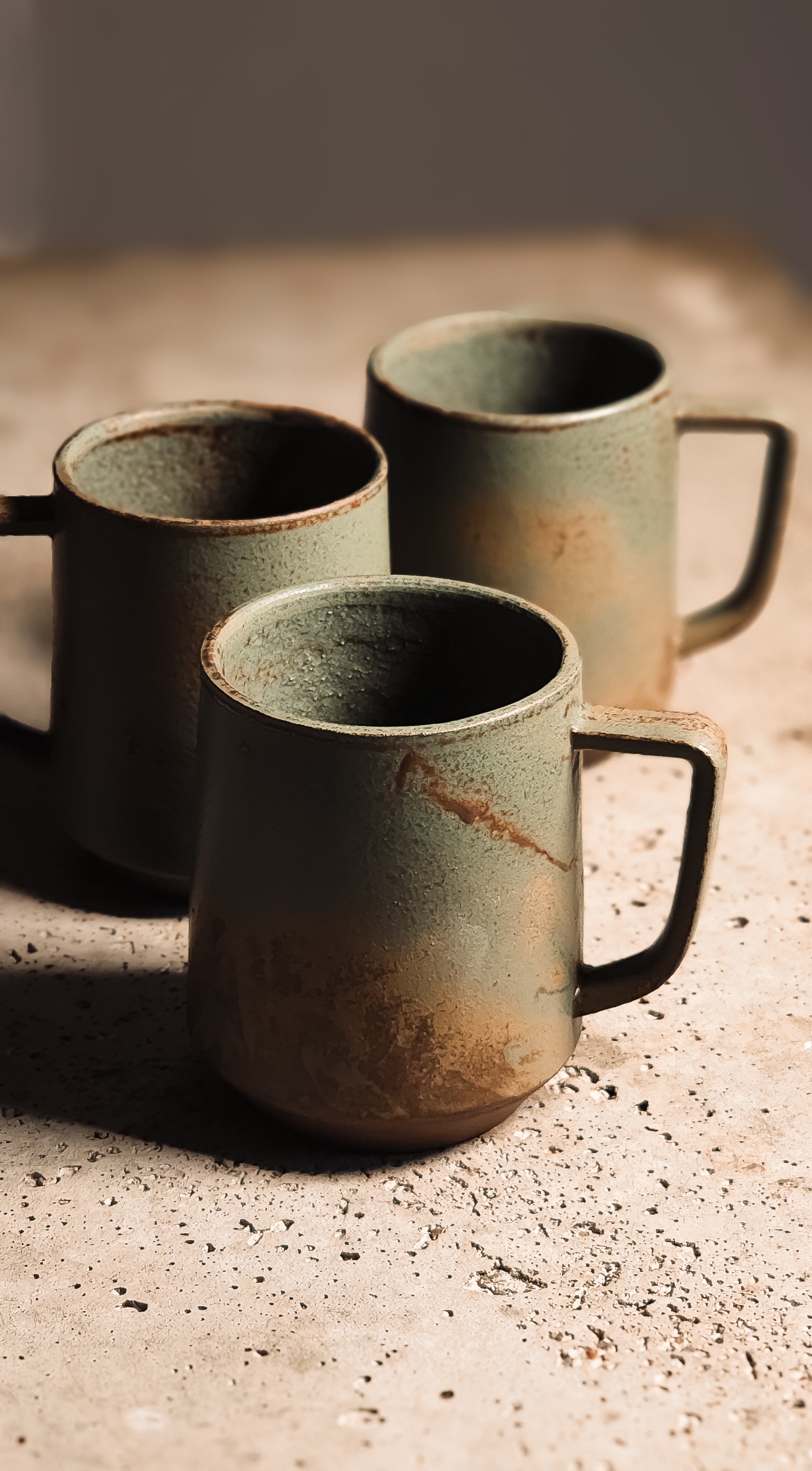 Textured sage green stoneware mug with earthy brown ombré and dark handle on a speckled surface.