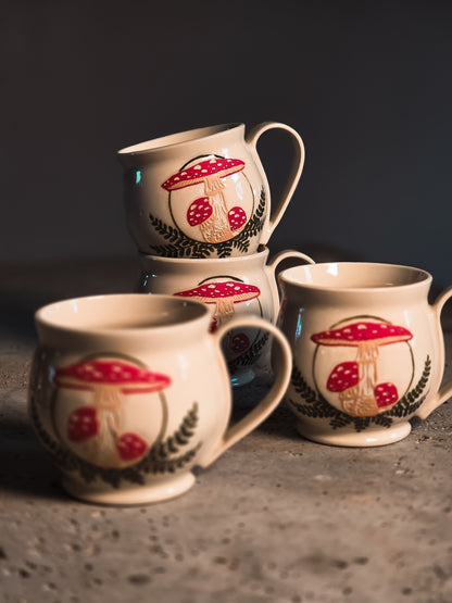 Cream ceramic Amanita Mushroom Mugs with red spotted mushroom and black fern design, stacked and individually displayed.