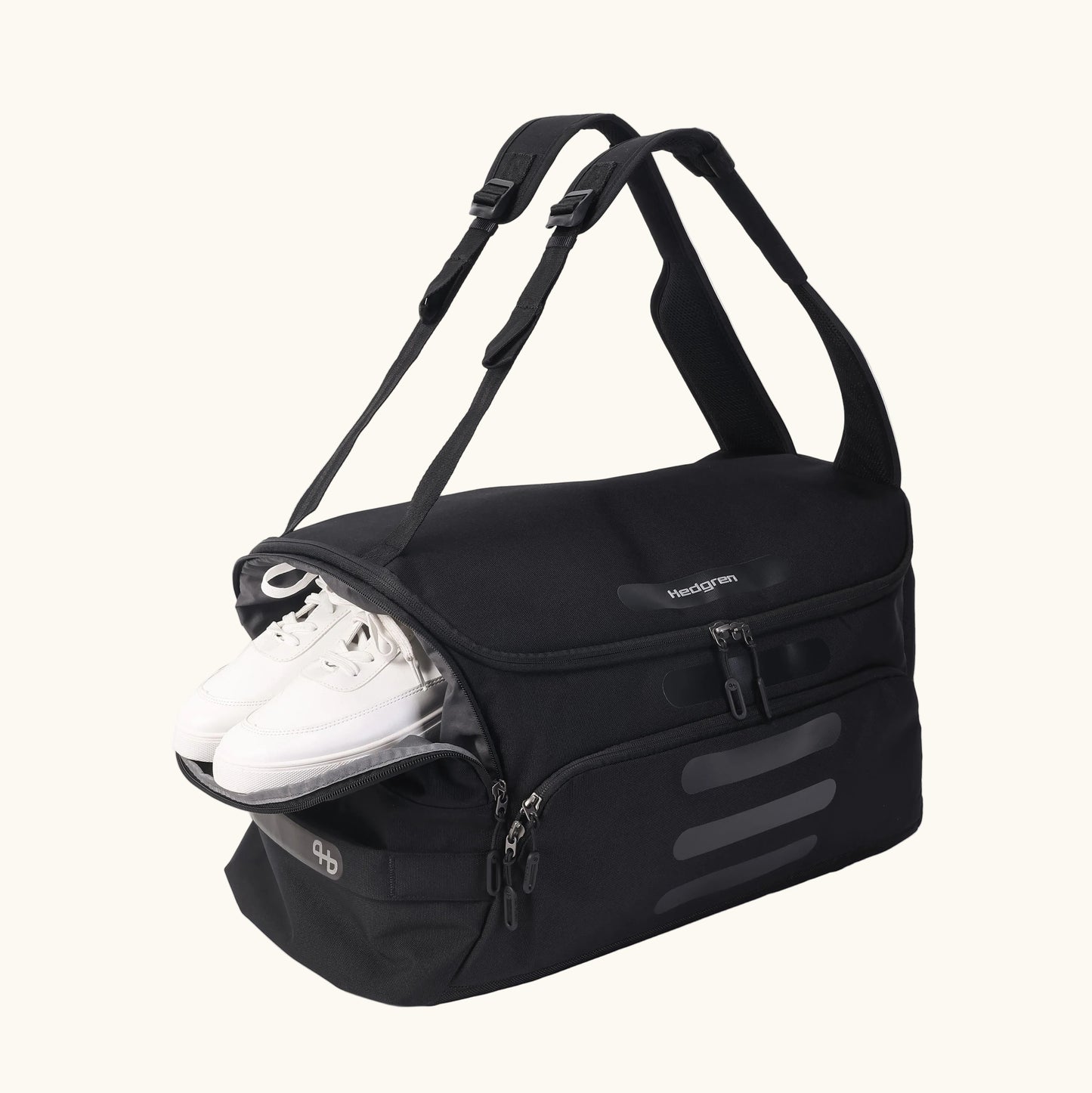 Black duffle bag by Hedgren with adjustable straps, multiple pockets, and white sneakers visible.