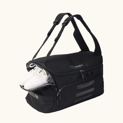 Black duffle bag by Hedgren with adjustable straps, multiple pockets, and white sneakers visible.