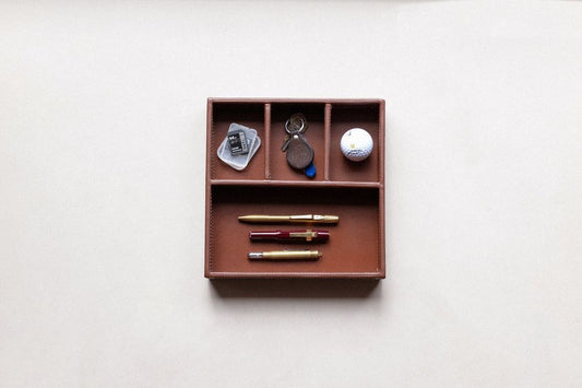 Brown leather supply tray with compartments holding three pens, keys, an SD card, and a golf ball.