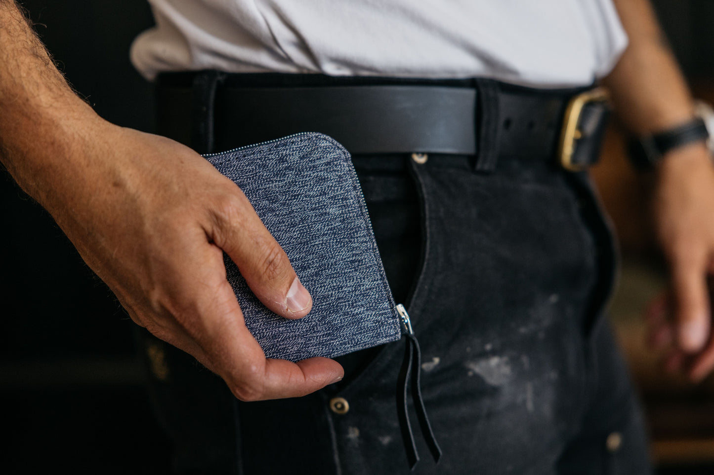 Indigo salt and pepper textile zip wallet held in a hand, being placed into a black pant pocket.