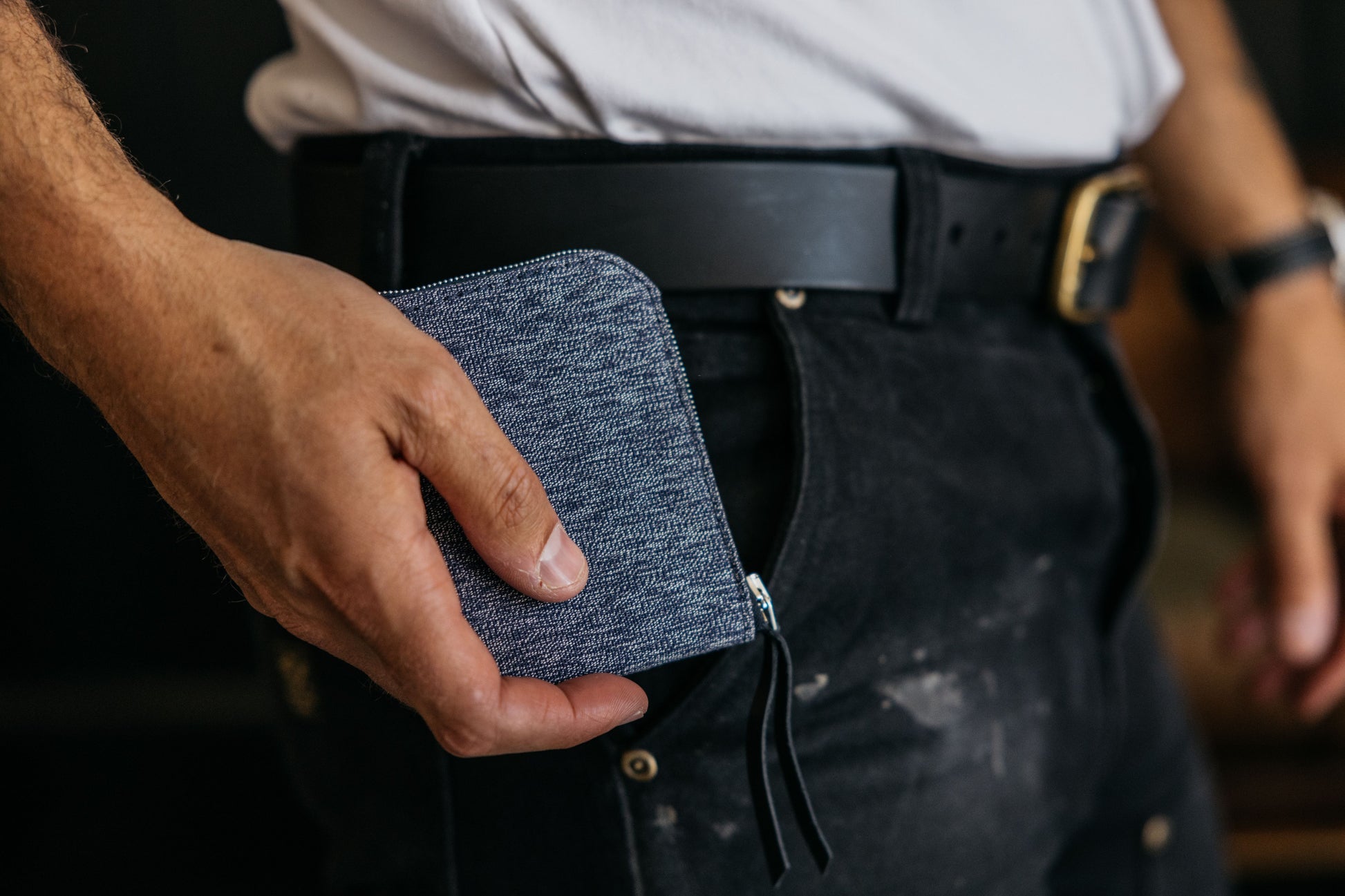 Indigo salt and pepper textile zip wallet held in a hand, being placed into a black pant pocket.