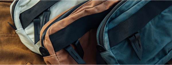 Three canvas bags in beige, brown, and blue with black zippers and straps, arranged side by side.