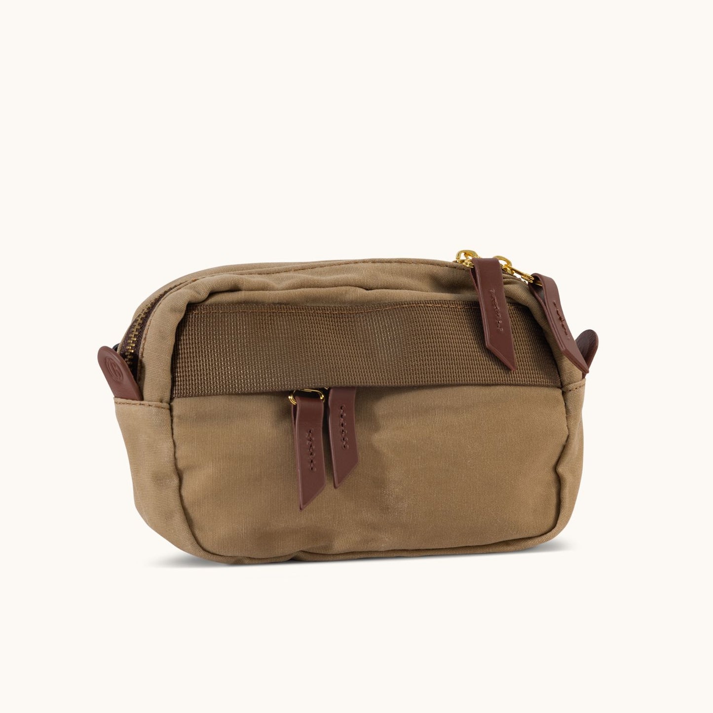 Tan waxed canvas mini crossbody bag featuring dark brown leather zipper pulls, gold hardware, and a front webbing strap, angled view.