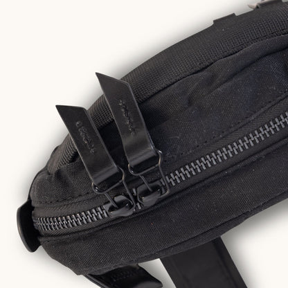 Black waxed canvas crossbody mini bag featuring two black leather zipper pulls and a dark grey zipper.