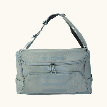 A green Hedgren Sojourn duffle bag with multiple compartments and a rolled-up design, featuring a shoulder strap and a top handle.