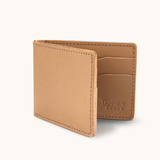 Utility bifold wallet in natural leather by Tanner Goods, open showing embossed logo, card slots, and stitching.