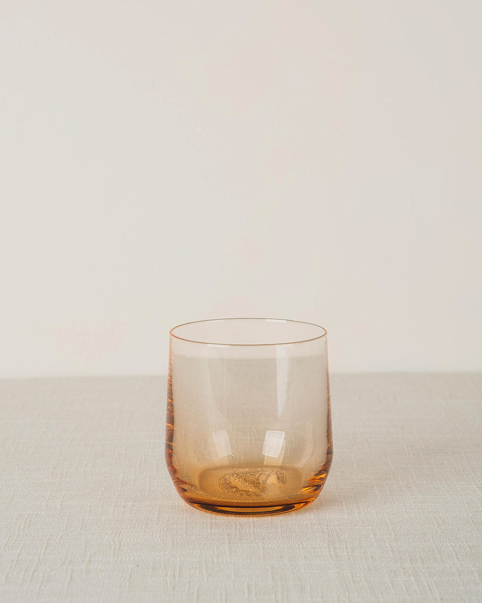 Amber glass cocktail glass with a smooth, curved design and textured base on a light fabric surface.