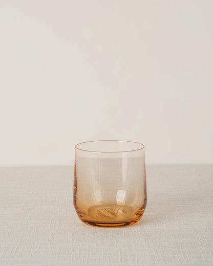 Amber glass cocktail glass with a smooth, curved design and textured base on a light fabric surface.