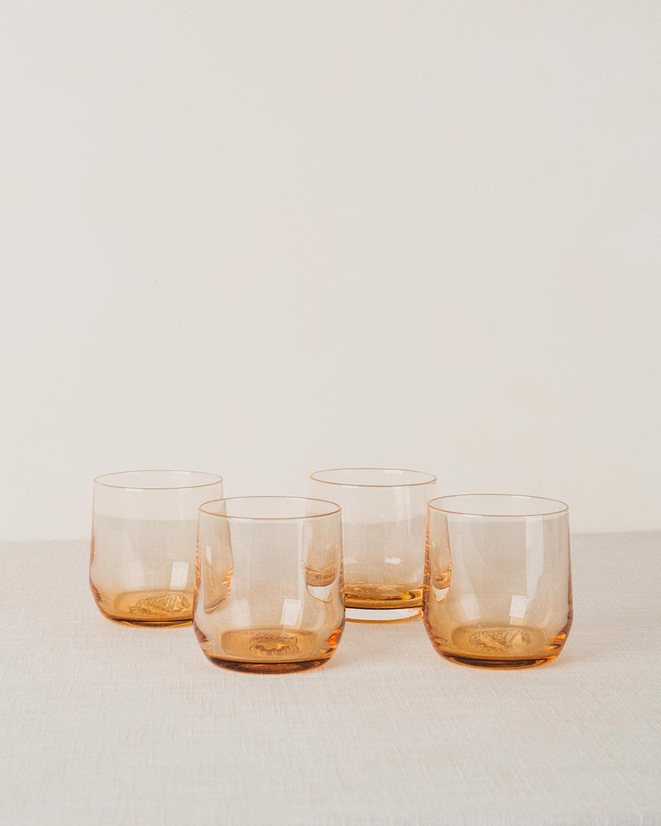 Four amber-tinted stemless cocktail glasses with an embossed pattern on the bottom, on a linen surface.