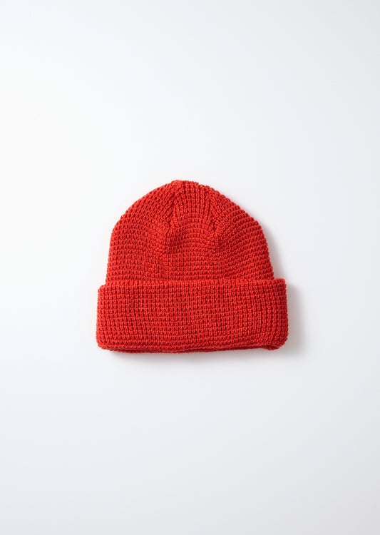 Red waffle knit watch cap with a folded brim, laid flat on a white background.