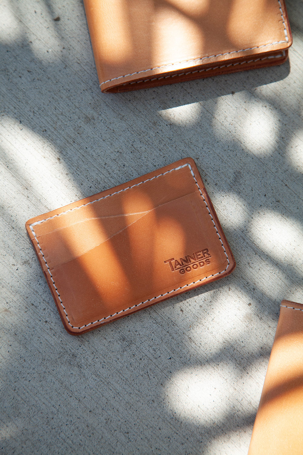 Golden leather card wallet by Tanner Goods with white contrast stitching, shown on concrete.