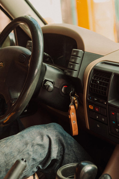 Saddle tan leather key lanyard with keys, hanging in a car's ignition.