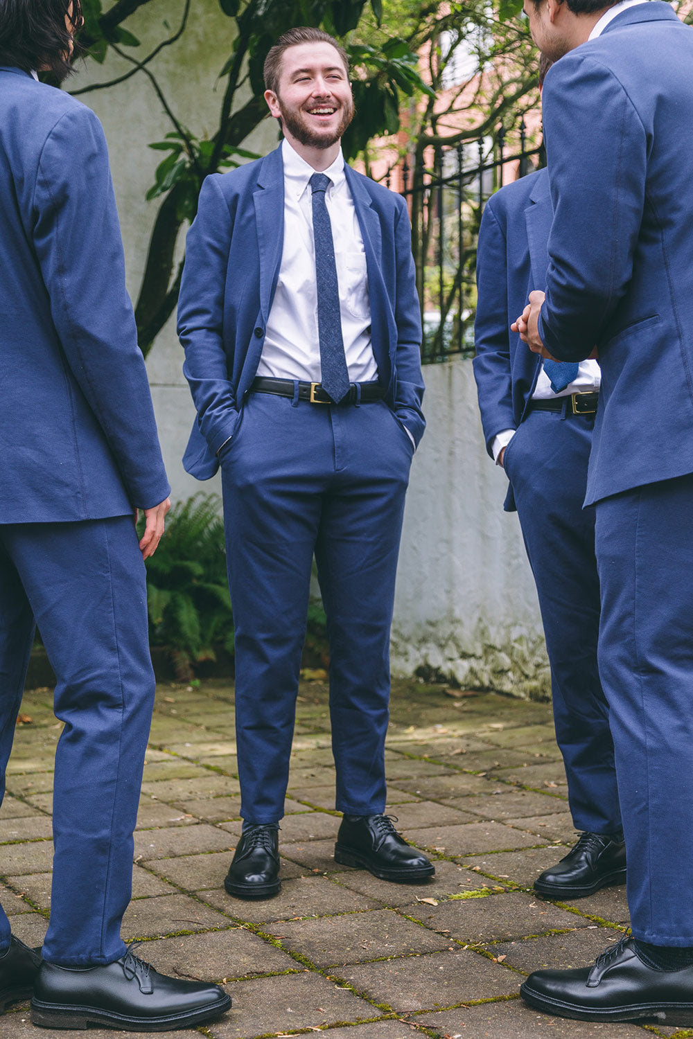Black dress belt with a gold E-shaped buckle worn by a man in a white shirt and blue suit.