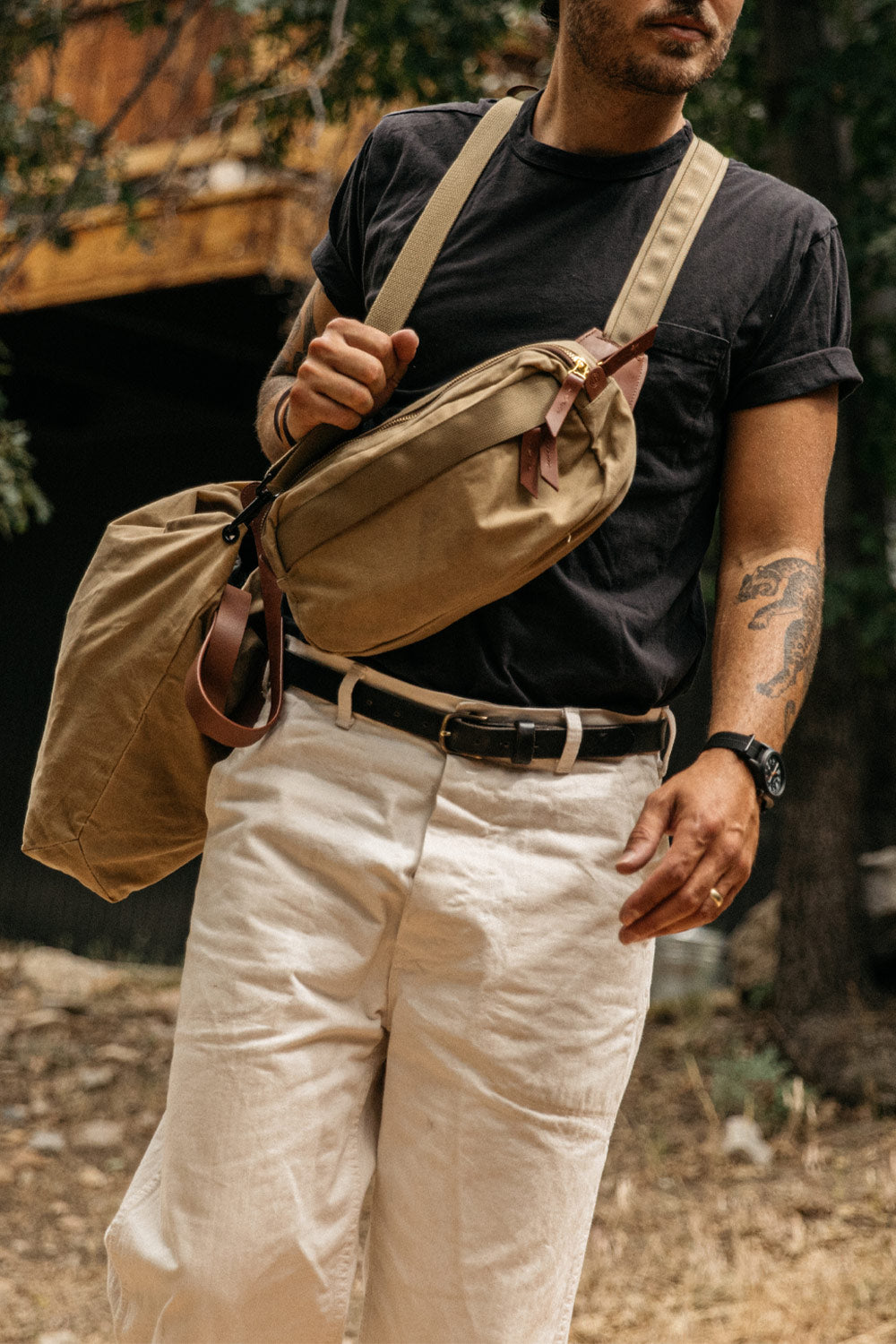 Black classic leather belt with a silver buckle, worn by a man in off-white trousers.