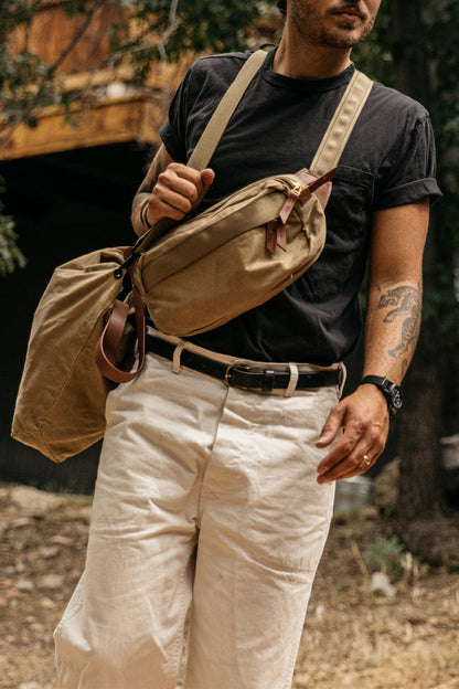 Black classic leather belt with a silver buckle, worn by a man in off-white trousers.