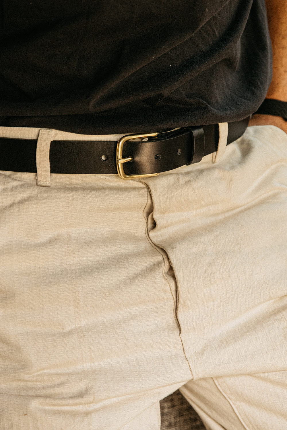 Classic black belt featuring a brass buckle, paired with light-colored trousers and a dark shirt.