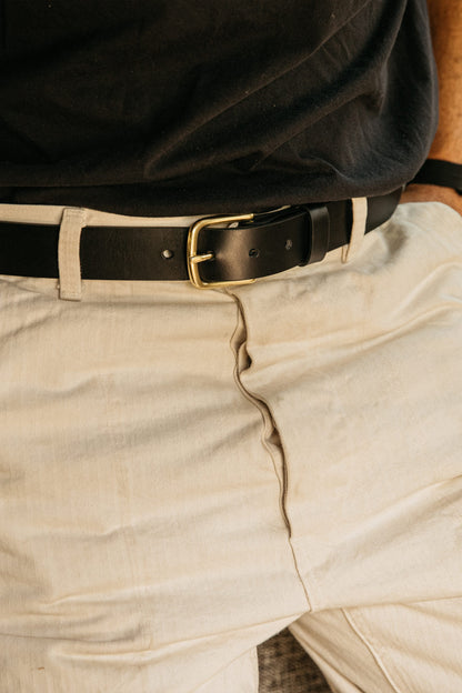 Classic black belt featuring a brass buckle, paired with light-colored trousers and a dark shirt.