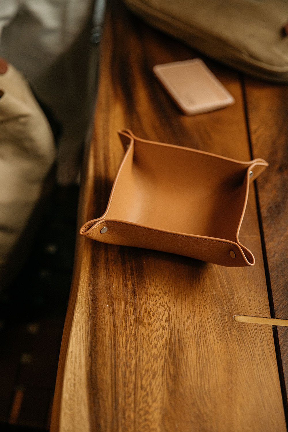 Recycled leather valet tray in saddle tan with riveted corners, resting on a wooden table.