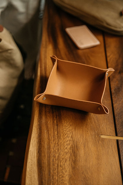 Recycled leather valet tray in saddle tan with riveted corners, resting on a wooden table.